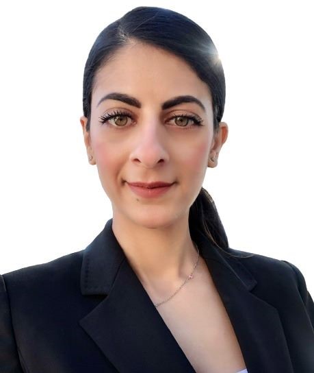 A woman with long dark hair tied back, wearing a black blazer and a delicate necklace, smiles slightly. She is looking directly at the camera with a white background behind her, exemplifying professionalism in careers.